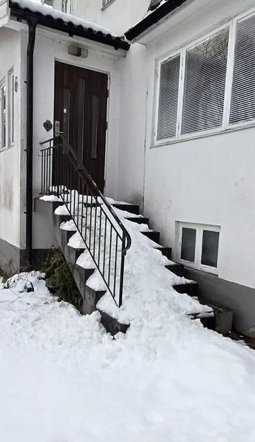 Snö vid trappan under det branta takfallet vid husets entré