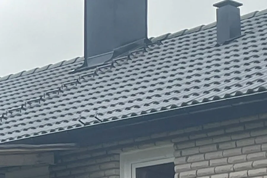 Skorsten inklädd med mörk plåt på tak med betongpannor