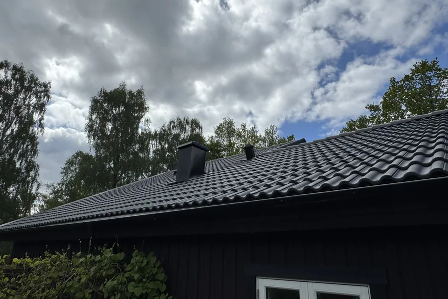 Skorstensbeslag och ventilationshuv på mörkt tak med takpannor
